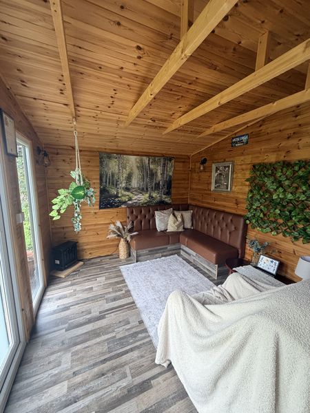 My therapy room: a calm wood-panelled cabin with a corner sofa, soft rug, plants and a large window